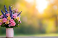 Fresh spring bouquet with pink roses, purple lavender and chrysanthemums in ceramic vase against soft bokeh background with golden sunlight glow.