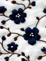 Navy blue embroidered flowers with brown stems and white centers on white fabric, creating elegant floral pattern for textile and fashion design.