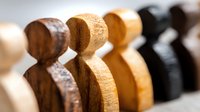 Wooden chess pawns in different natural wood tones arranged in row showing texture and grain detail. Selective focus creates artistic depth of field effect.