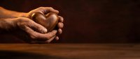 Male hands clasped together in prayer position on wooden table surface with warm lighting creating peaceful spiritual atmosphere for meditation concepts.