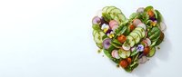 Fresh vegetable salad arranged in heart shape with cucumber, radish, tomato and greens on white background for healthy eating and nutrition content.