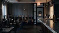 Empty restaurant interior with chairs stacked on tables during closing time, modern dining establishment with dark walls and ambient lighting.