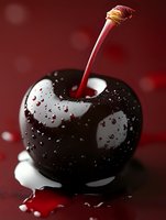 Fresh dark cherry with water drops on glossy surface against deep red background, dramatic lighting highlights natural moisture and reflections.