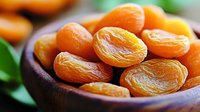 Dried apricots in wooden bowl with green leaves, close up view of healthy organic dried fruit snack. Natural sweet preserved food photography.