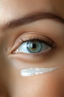 Close-up of green eye with moisturizer cream streak on cheek showing skincare and beauty concept. Natural makeup with long eyelashes and defined brows.