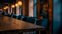 Wooden table in focus with blurred modern restaurant interior, teal chairs, and warm pendant lighting in background for hospitality and dining concepts.