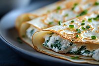 Thin golden crepes filled with creamy ricotta and spinach mixture, garnished with fresh chopped chives on dark plate, close up view of homemade savory crepes.