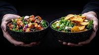 Fresh poke bowls with raw tuna, salmon, avocado and vegetables in black bowls against dark background. Hands holding healthy Asian food serving.
