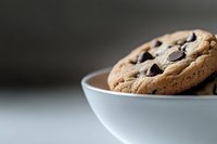 Fresh chocolate chip cookie in white ceramic bowl against blurred background, showcasing melty chocolate chips and golden-brown texture. Perfect for food marketing.