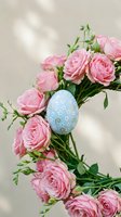 Pink roses bouquet with decorative blue Easter egg on neutral background with soft natural lighting shadows for spring holiday celebrations.