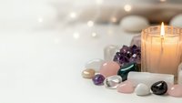 Spa wellness setup with healing crystals, lit candle and smooth stones creating peaceful meditation atmosphere for relaxation and self-care rituals.