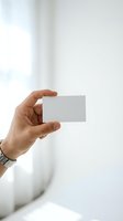 Male hand holding blank white business card mockup against bright window background for branding and corporate identity design projects.