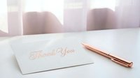 Elegant thank you card with rose gold pen on white desk in soft natural light creating warm professional atmosphere for gratitude expression.