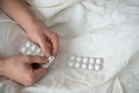 Person holding white medication pills in blister packs on bed sheets for healthcare and treatment concept.