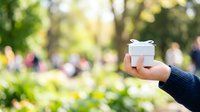 Unrecognizable person holding white gift box with ribbon in sunny park setting, perfect for holiday, celebration, and present-giving concepts.