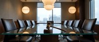 Modern corporate boardroom with leather chairs around polished conference table and city view through large windows for business meetings and presentations.