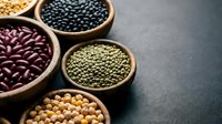 Assorted legumes and pulses in wooden bowls including chickpeas, lentils, black beans and kidney beans on dark surface for cooking and nutrition.