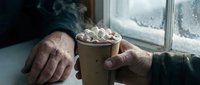 Elderly hands holding steaming hot chocolate with marshmallows by frosted winter window. Cozy seasonal comfort drink for cold weather relaxation and warmth.