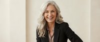 Confident mature Caucasian businesswoman with silver hair laughing in black blazer, professional corporate portrait for leadership and success concepts.