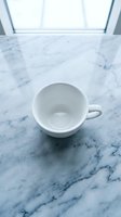 Empty white ceramic cup on marble surface with natural light from window above, suitable for beverage, coffee, tea, and kitchen design projects.