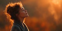 Young woman with curly hair enjoying peaceful moment in warm golden sunlight, eyes closed in meditation and gratitude during beautiful sunset hour.