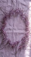 Delicate dried baby's breath flowers arranged in oval frame on soft purple linen fabric background for wedding invitations and romantic design projects.