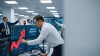 Businessman in white shirt analyzing market recovery chart with red upward arrow on digital display in modern office environment with colleagues in background.