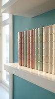 Vintage leather bound books arranged on white floating shelf against turquoise wall in modern home library interior design for reading room decoration.