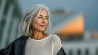 Confident mature woman with silver hair smiling outdoors at sunset, representing aging gracefully, self-assurance, and positive lifestyle choices for seniors.