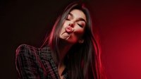 Young Asian woman with long dark hair in plaid shirt posing sensually against red background with dramatic lighting and shadows creating moody atmosphere.