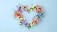 Heart-shaped floral wreath with colorful paper flowers on light blue background for romantic decorations and craft projects.
