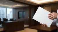 Close-up of male hand holding blank white paper in modern office interior with city skyline view through windows, suitable for business presentations and corporate messaging.