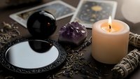Mystical fortune telling setup with tarot cards, crystal ball, amethyst cluster, burning candle and sage bundle for spiritual guidance and divination practices.
