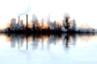 Industrial cityscape silhouette with factory chimneys and smoke reflected in calm water at sunrise, creating atmospheric urban waterfront scene.