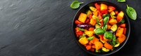 Fresh colorful bell peppers and basil leaves in black bowl on dark stone background, healthy vegetarian food ingredients for cooking, top view.