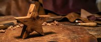 Handcrafted wooden star decoration on rustic workbench with traditional woodworking tools and wood shavings creating warm artisan workshop atmosphere.
