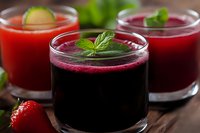 Fresh fruit and vegetable smoothies in glass cups garnished with mint leaves and lime slice, showcasing vibrant red and purple colors on wooden surface.