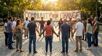 Diverse group of people holding hands in circle around Community for Change banner in sunny park setting promoting unity and social activism.