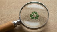 Magnifying glass revealing green recycling symbol on kraft paper surface, representing environmental sustainability and eco-friendly practices for conservation awareness.