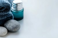 Spa wellness composition with smooth massage stones, turquoise aromatherapy oil bottle and soft grey towel on light background with copy space.