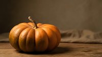 Fresh orange pumpkin with curved stem on rustic wooden table against dark background for autumn harvest seasonal decoration and cooking.