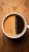 White ceramic cup of fresh hot cocoa with frothy surface split in light and dark halves on brown textured background, top view composition.