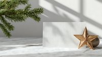 Minimalist Christmas composition with golden star decoration, pine branches, and blank card on white surface with soft window shadows.