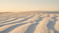 Soft golden sand dunes with natural wind-carved ripple patterns creating textured waves across desert landscape during warm sunset light.
