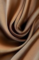 Smooth waves of luxurious brown silk fabric create elegant curves and folds, showcasing rich texture and gentle shadows in a minimalist abstract composition.