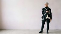 Senior woman with short gray hair, Caucasian ethnicity, wearing formal black blazer and trousers with cream blouse, standing confidently in minimalist studio setting for corporate and business use.