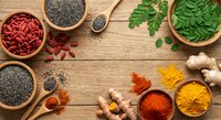 Superfood ingredients arranged on rustic wooden background with goji berries, chia seeds, moringa leaves, turmeric powder and ginger root for healthy cooking.