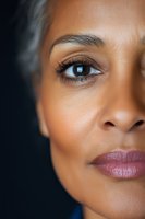 Close-up portrait of young African American woman with natural makeup, flawless skin, and expressive brown eyes against dark background.