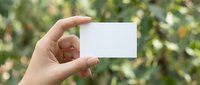 Hand holding a blank white business card against a blurred green nature background, mockup with copy space for branding design.
