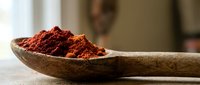 Red chili powder spice in wooden spoon on kitchen counter. Cooking ingredient for spicy recipes and culinary preparations.
